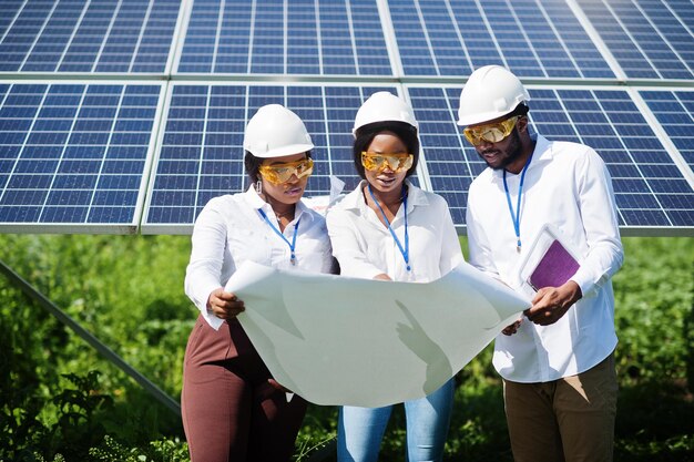 Técnico americano africano verifica a manutenção dos painéis solares Grupo de três engenheiros negros reunidos na estação solar