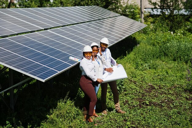 Técnico americano africano verifica a manutenção dos painéis solares Grupo de três engenheiros negros reunidos na estação solar