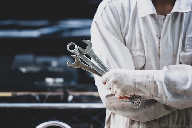 Foto grátis técnico de automóveis, vestindo um uniforme branco, de pé e segurando uma chave inglesa, que é uma ferramenta essencial para um mecânico