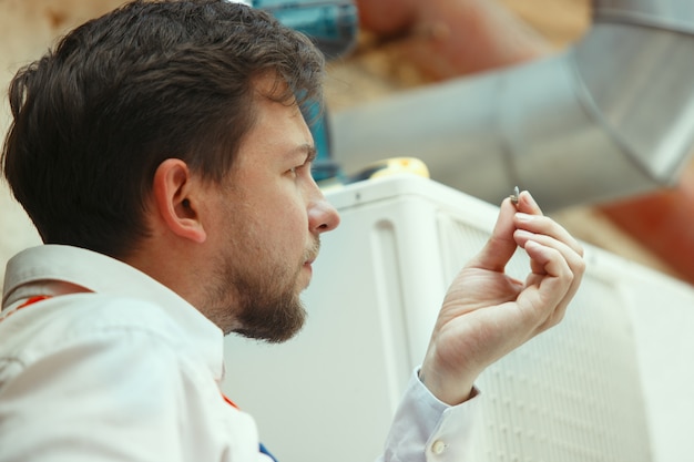 Técnico de HVAC trabalhando em uma peça de capacitor para unidade de condensação. Trabalhador do sexo masculino ou reparador de uniforme reparando e ajustando o sistema de condicionamento, diagnosticando e procurando problemas técnicos.