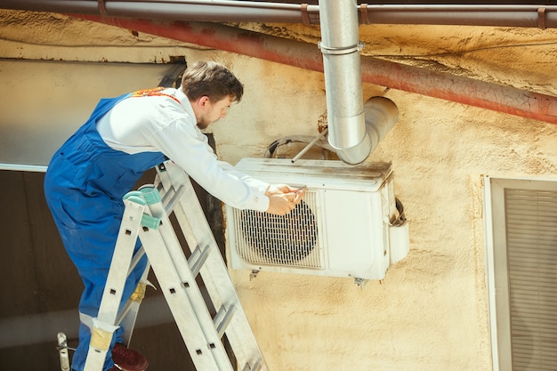 Foto grátis técnico de hvac trabalhando em uma peça de capacitor para unidade de condensação. trabalhador do sexo masculino ou reparador de uniforme reparando e ajustando o sistema de condicionamento, diagnosticando e procurando problemas técnicos.