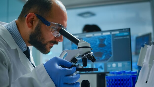 Técnico de laboratório examinando amostras e líquidos usando microscópio em laboratório equipado