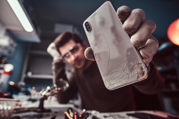 Técnico eletrônico mostrando um smartphone moderno com um corpo quebrado em uma oficina