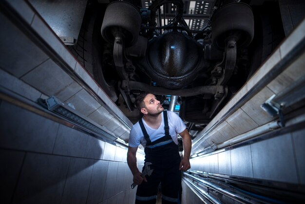 Técnico mecânico profissional sob o caminhão procurando um vazamento de óleo em uma oficina mecânica