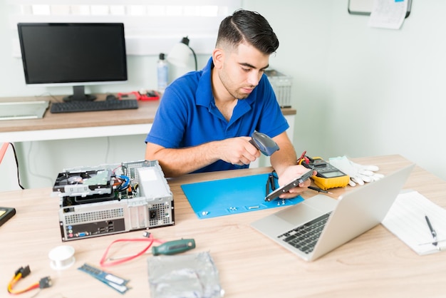 Técnico trabalhador digitalizando o código de barras de um componente quebrado antigo para procurar uma peça de reposição na oficina