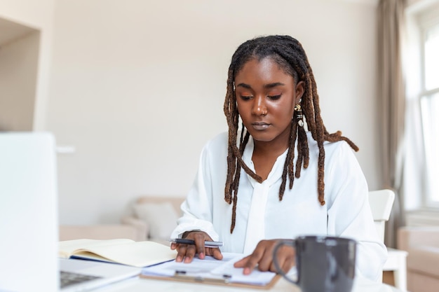 Tecnologia de trabalho remoto e conceito de pessoas feliz sorrindo jovem empresária negra com computador portátil e papéis trabalhando em home office