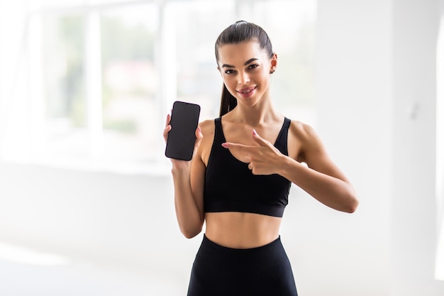 Tecnologia esportiva e conceito de estilo de vida ativo Desportista atraente satisfeita, apontando a tela do smartphone com o dedo, recomenda o aplicativo rastreador de treino móvel