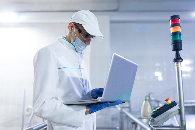 Foto grátis tecnólogo com laptop nas mãos faz uma configuração da linha de produção enquanto está no departamento de fábrica de laticínios