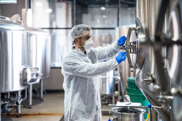 Tecnólogo em uniforme de proteção usando máscara de rede para o cabelo e luvas fechando reservatório de tanque industrial