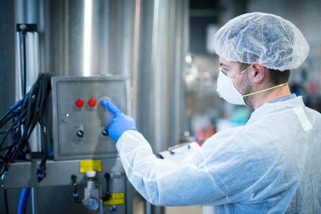 Tecnólogo em uniforme protetor branco com rede para cabelo e máscara operando em máquina industrial para processamento de alimentos
