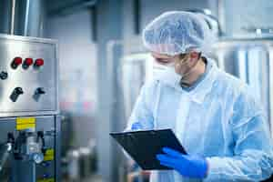 Foto grátis tecnólogo especialista em uniforme de proteção com rede e máscara tomando parâmetros de máquina industrial em planta de produção de alimentos