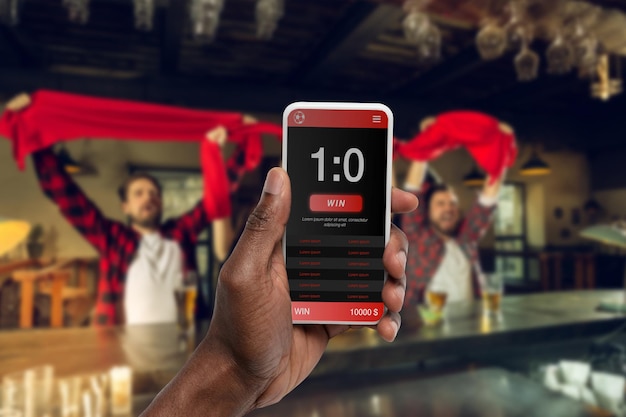 Tela do dispositivo com aplicativo móvel para apostas e pontuação, torcendo amigos, fãs em segundo plano