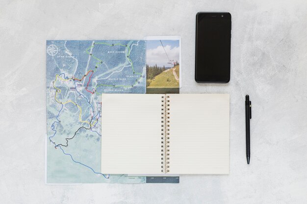 Telefone celular, caneta e caderno espiral no mapa sobre o fundo