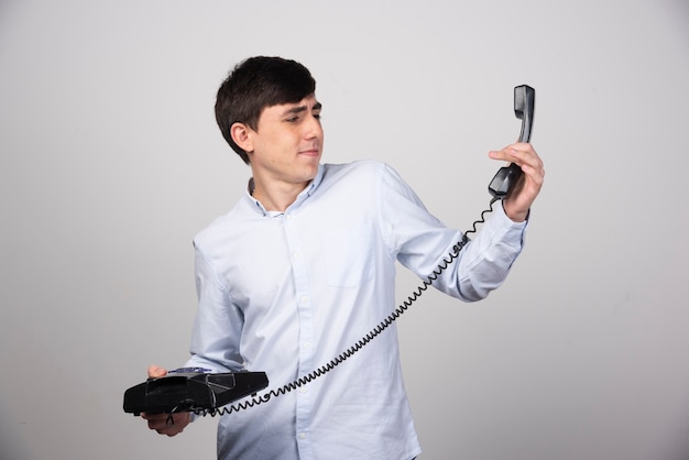 Telefone fixo preto na mão de um homem na parede cinza.