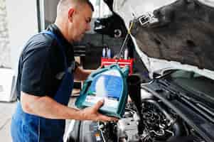 Foto grátis tema de reparação e manutenção de automóveis mecânico de uniforme trabalhando em serviço automotivo derramando óleo de motor novo