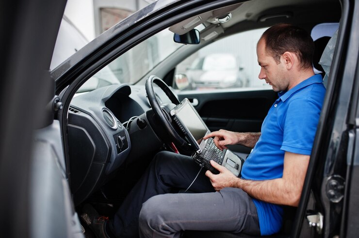 Foto grátis tema de reparo e manutenção de carros mecânico elétrico de uniforme trabalhando em serviço automotivo fazendo diagnósticos de carros usando dispositivo obd com laptop