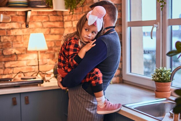 Tempo do pai no halloween. Menina bonitinha na maquiagem de coelho e chapéu sentado nas mãos de seu pai na cozinha estilo loft de manhã.