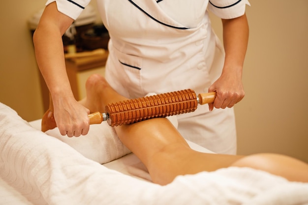 Terapeuta irreconhecível realizando maderoterapia nas pernas da mulher durante o tratamento de massagem no spa
