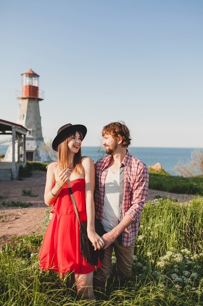 Terno jovem casal elegante apaixonado no campo, estilo indie hippie boêmio, férias de fim de semana, roupa de verão, vestido vermelho, grama verde, de mãos dadas, sorrindo