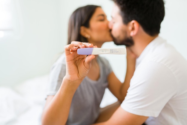 Teste de gravidez positivo. jovem latina e homem apaixonado beijando com paixão depois de descobrir que vão ser pais