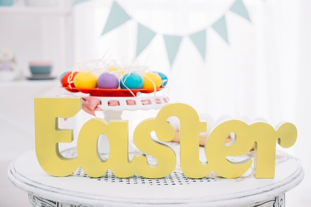 Texto amarelo de Páscoa na frente de ovos de Páscoa coloridos no cakestand