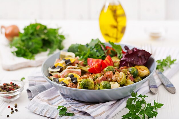 Tigela com macarrão Farfalle, couve de Bruxelas com bacon e salada de legumes frescos