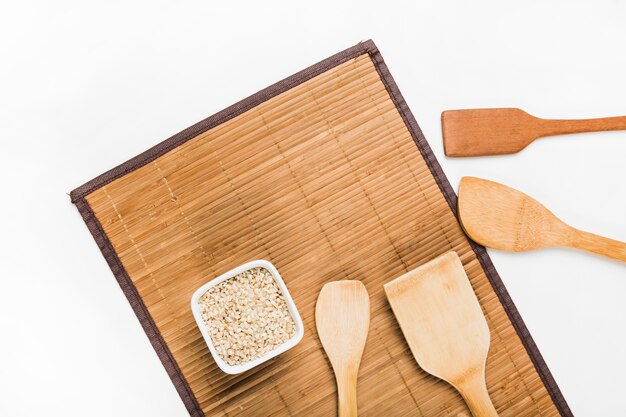 Tigela de arroz cru plana e espátulas de madeira em placemat sobre fundo branco