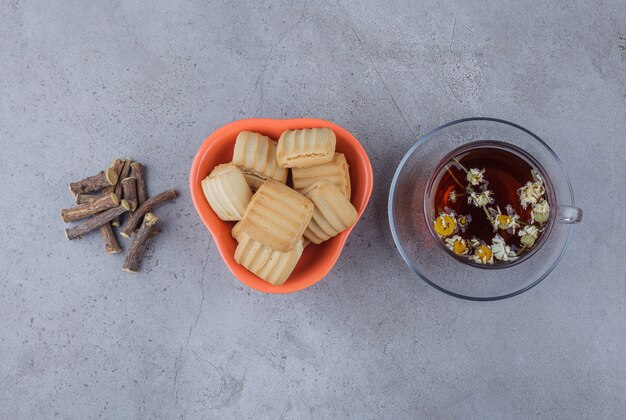 Tigela de biscoitos doces e copo de chá quente na superfície da pedra.