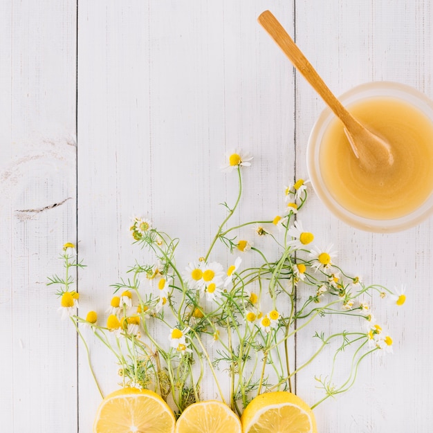 Foto grátis tigela de coalhada de limão; flores de camomila e limão na prancha de madeira