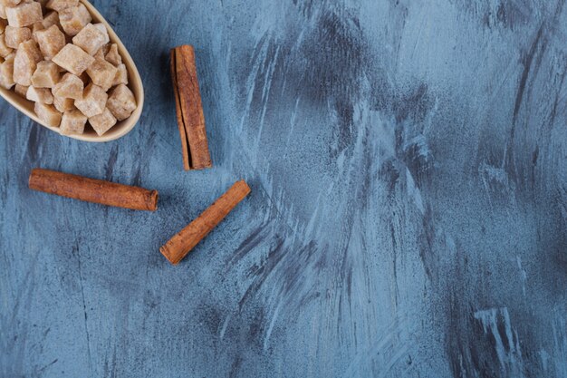 Foto grátis tigela de cubos de açúcar mascavo e paus de canela na superfície azul.