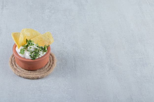 Tigela de iogurte com verduras e batatas fritas na pedra.