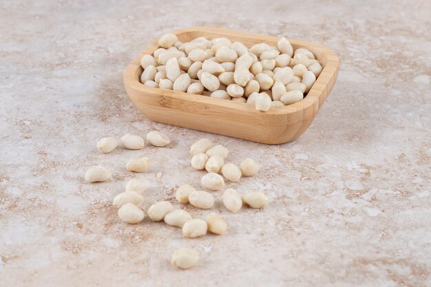 Tigela de madeira com grãos de amendoim colocada na mesa de mármore.