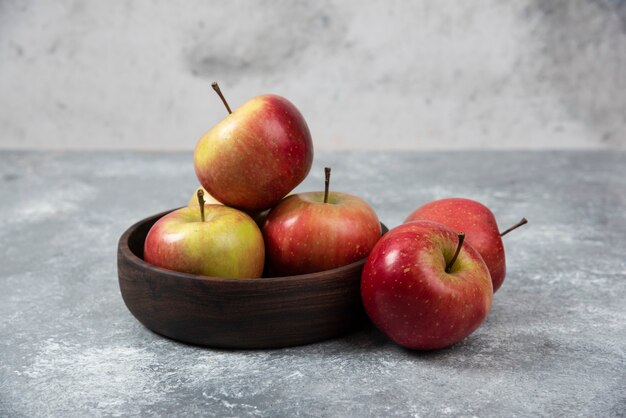Tigela de madeira com maçãs frescas e saborosas na superfície de mármore.