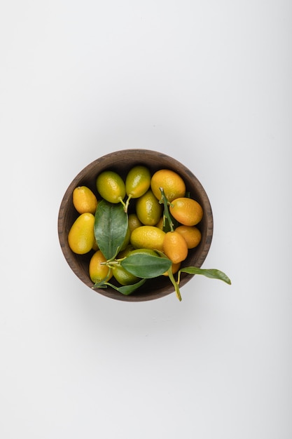 Tigela de madeira de kumquats amarelos com folhas brancas.