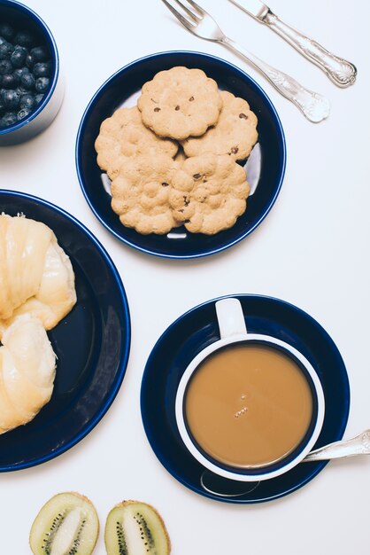 Tigela de mirtilos; biscoitos; kiwi e xícara de café sobre fundo branco