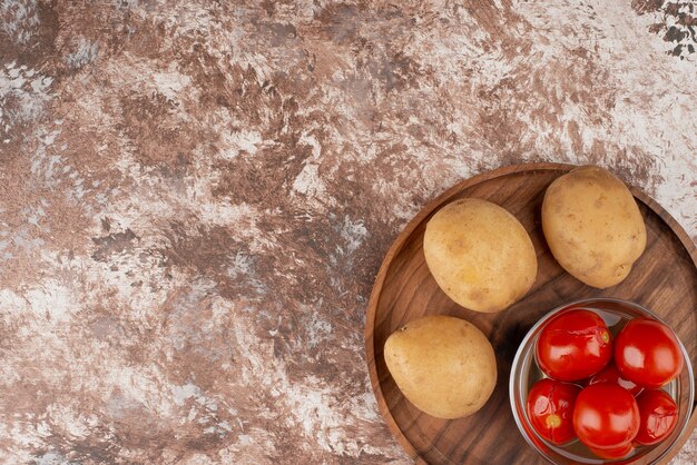 Tigela de tomates em conserva e batatas cozidas na mesa de mármore.