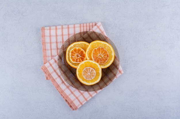 Tigela de vidro com fatias de laranja frescas e secas na mesa de pedra.