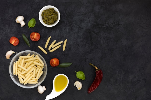 Tigela de vidro de macarrão garganelli com molho; cogumelo; manjericão; tomates; pimentão vermelho e dente de alho no pano de fundo texturizado preto