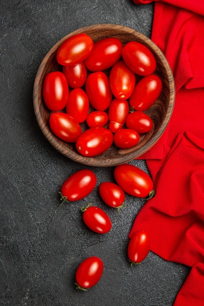 Tigela de vista superior com toalha vermelha de tomate cereja e tomate cereja em fundo escuro