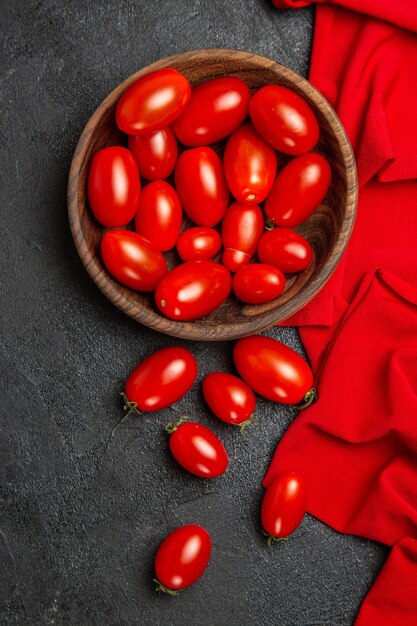 Tigela de vista superior com toalha vermelha de tomate cereja e tomate cereja em fundo escuro