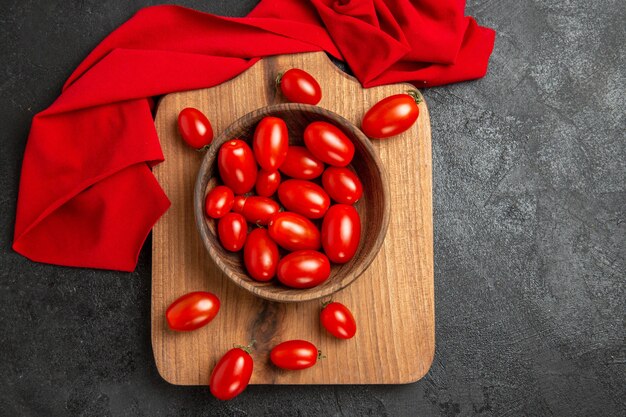 Tigela de vista superior com tomate cereja e toalha vermelha em uma tábua de cortar em fundo escuro