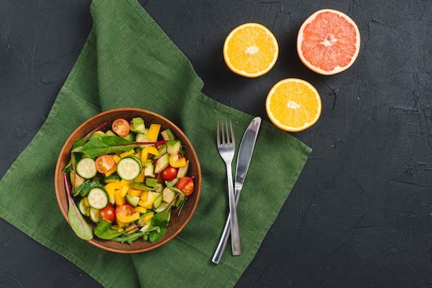 Tigela fresca de salada de legumes; laranjas e toranjas em fundo preto de concreto