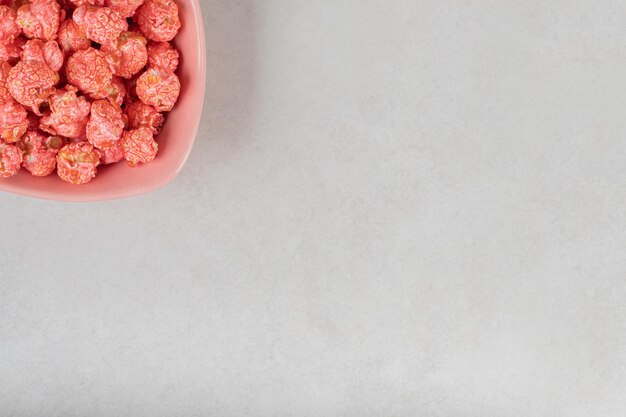 Tigela rosa cheia com uma porção de doces de pipoca na mesa de mármore.