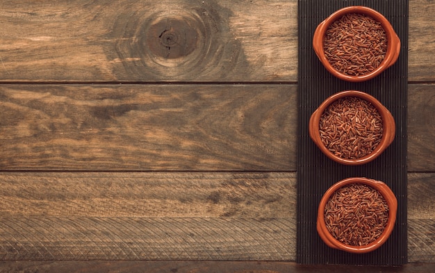 Tigelas de arroz jasmim vermelho cru no placemat sobre o fundo de madeira