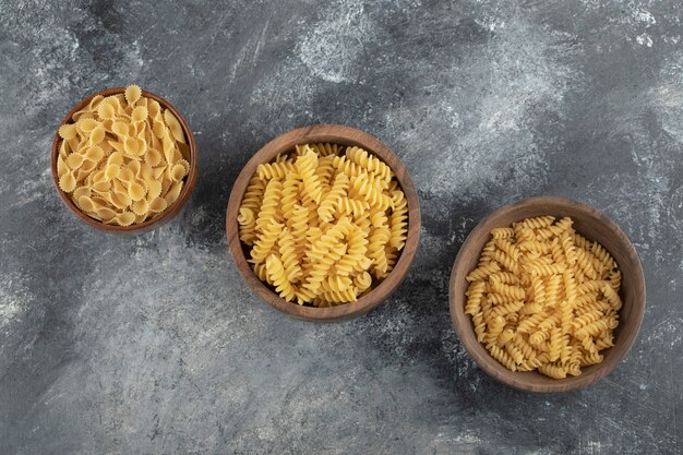 Tigelas de madeira cheias de massa Fusilli seca crua e farfalle tonde.
