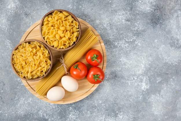 Tigelas de massa crua, ovos e tomates frescos na superfície de mármore.