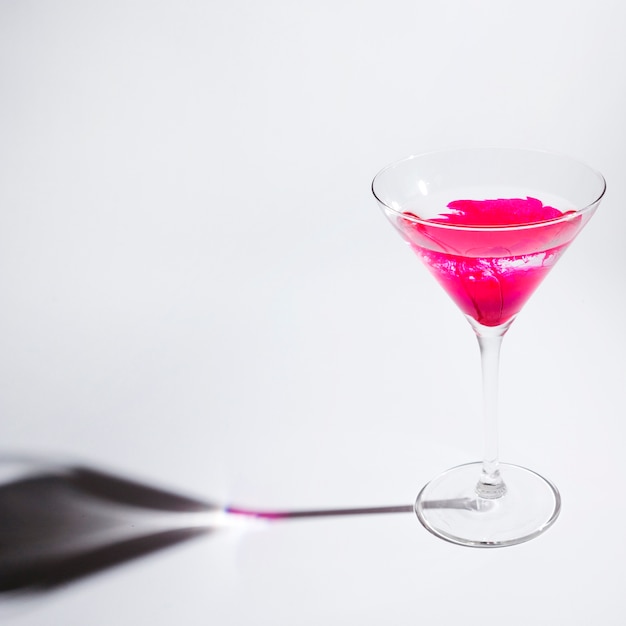 Tinta rosa dissolvendo no copo de martini contra fundo branco