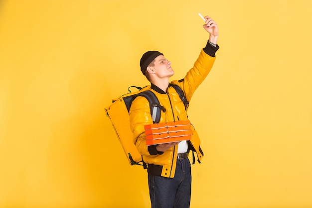 Tirando selfie, vlog. Emoções de entregador caucasiano em amarelo