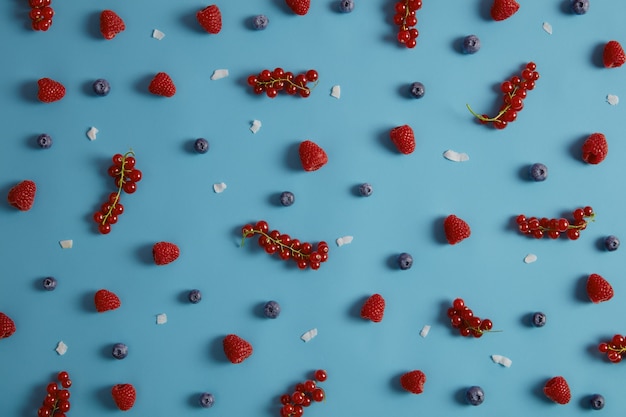 Tiro acima de saborosas frutas maduras apetitosas para comer ou fazer sobremesas. Pedaços de groselha, mirtilo e coco frescos de framboesa sobre fundo azul. Misture frutas para uma alimentação saudável.