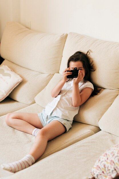 Tiro completo garota no sofá com câmera fotográfica
